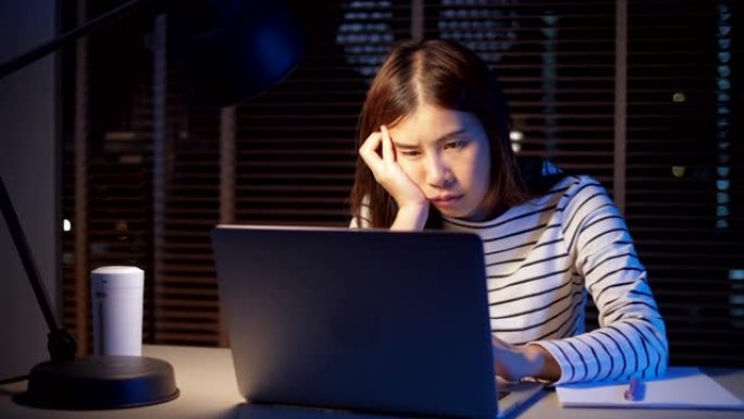 精疲力竭的女人坐在家里的办公桌前在笔记本电脑上工作