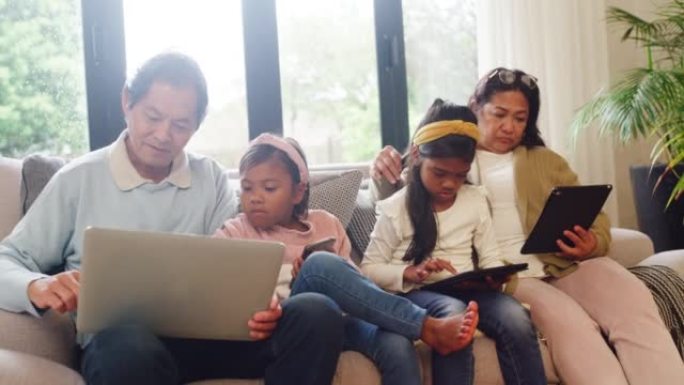 亚洲儿童和祖父母坐在沙发上沉迷于现代技术。绑定时使用无线设备的多代系列。教祖父如何使用互联网的孩子