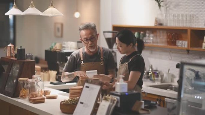 亚洲华人高级男咖啡馆老板在酒吧柜台咖啡店展示他的女儿食物菜单