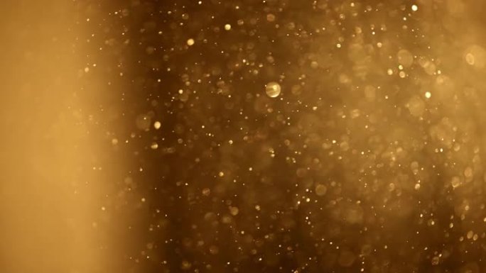 闪亮的金色粒子抽象背景。模糊的散景背景的金尘颗粒慢慢漂浮在空中。神奇的仙女背景