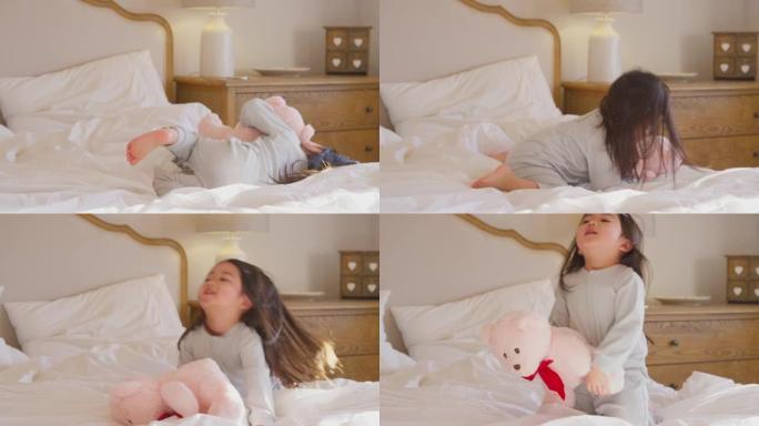 年轻女孩在家穿着睡衣在床上玩耍，拥抱着慢动作拍摄的泰迪熊