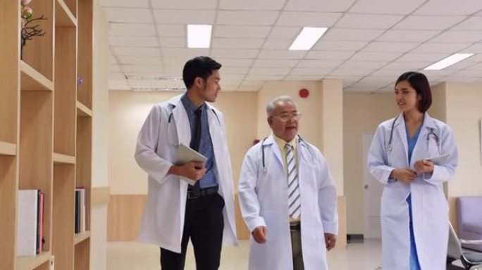 亚洲资深男性医学教授走过医院走廊，向现代医院大楼的医疗团队谈论患者的健康。医院概念。