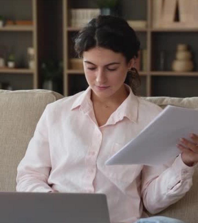 微笑的女人坐在带笔记本电脑的沙发上处理文件