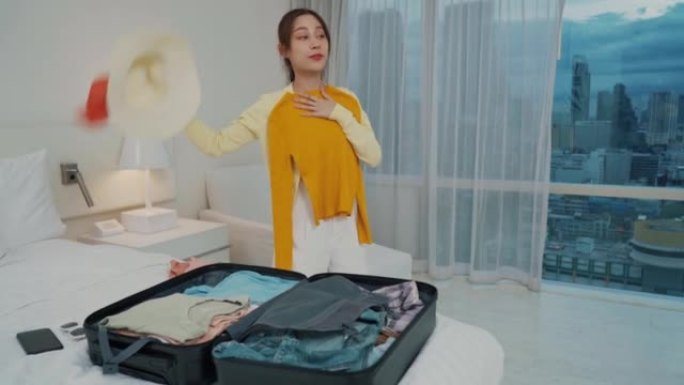 亚洲妇女打开行李，在卧室里尝试玻璃衣服