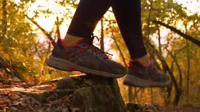 镜头耀斑: 女人在金色的秋天日落时下坡徒步旅行时踩在岩石上。