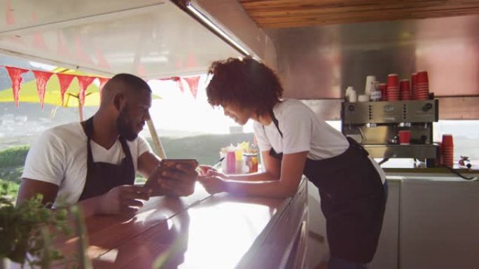 非裔美国夫妇穿着使用数字平板电脑的围裙，并在餐车上做笔记