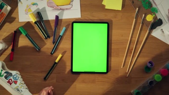 千禧一代设计师坐在办公桌前，在绿屏色度键平板电脑上工作的顶部特写视图。具有新鲜想法概念的有创造力的人