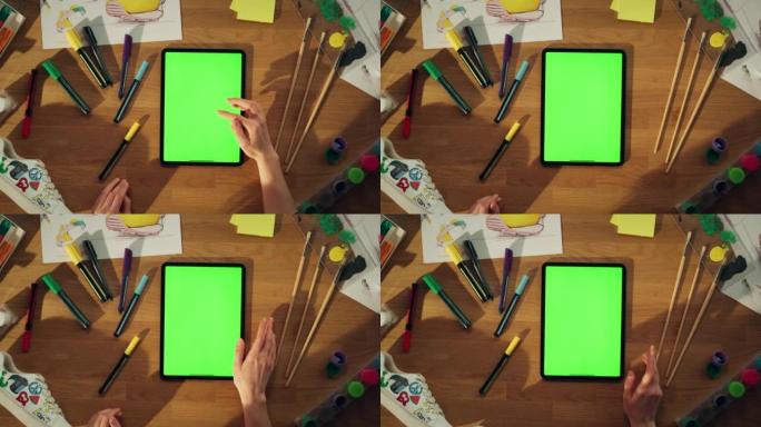 千禧一代设计师坐在办公桌前，在绿屏色度键平板电脑上工作的顶部特写视图。具有新鲜想法概念的有创造力的人