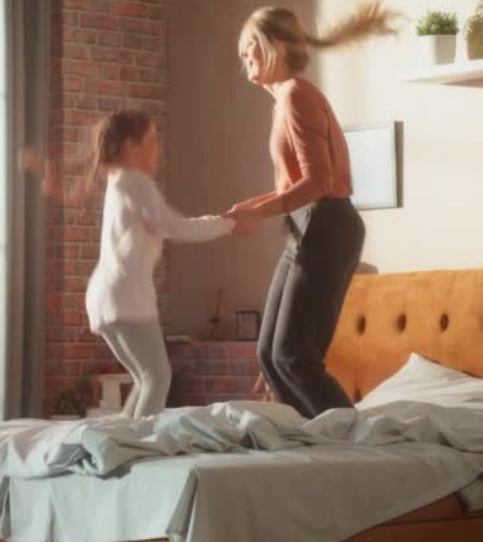 垂直屏幕: 可爱的小女儿和年轻的母亲在家里玩得开心。在家里愉快地玩耍，在时尚的阁楼公寓里跳上床。快乐
