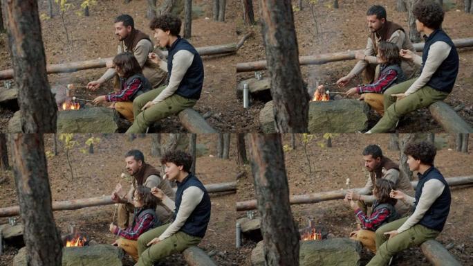 父母和可爱的孩子烤棉花糖，坐在篝火旁聊天