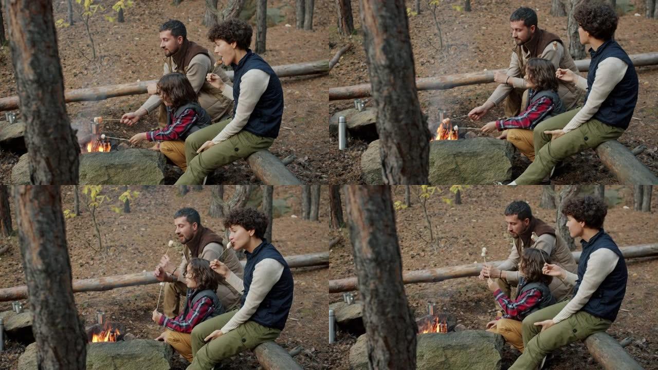 父母和可爱的孩子烤棉花糖，坐在篝火旁聊天