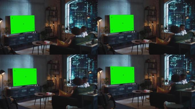黑人夫妇花时间在家里，坐在沙发上，拥抱着，看着绿屏上令人兴奋的电视。男女朋友聊天，聊天，八卦，玩得开