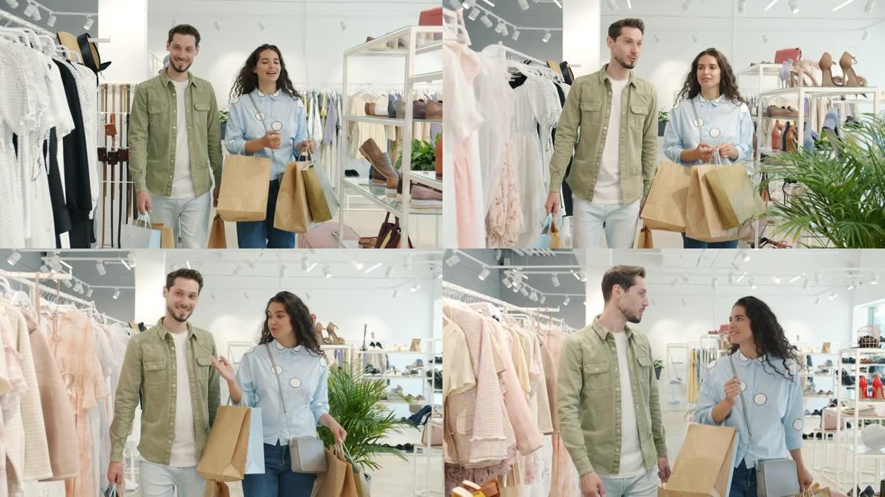 幸福的夫妇走在商店里的慢动作，拿着袋子说话，微笑着看着衣架上的衣服