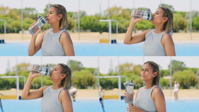 混合种族曲棍球运动员在训练时从瓶子里喝水。严肃而专注的年轻拉丁裔女孩在运动练习中休息一下，补充水分，