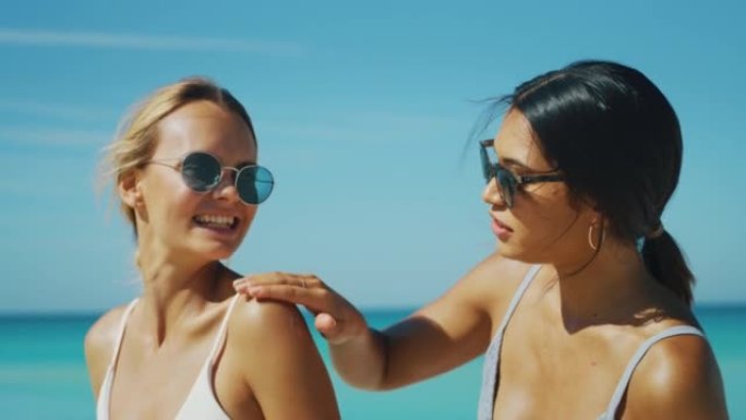 戴着太阳镜的快乐年轻女友的慢动作很有趣，可以在海滩度假期间涂上防晒霜或晒黑乳液来照顾自己的皮肤。