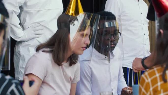 特写白人年轻女子戴着新型冠状病毒肺炎面具和塑料面罩与多民族朋友庆祝生日。