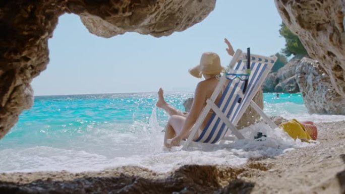 超级SLO MO女人在田园诗般的偏远海滩上海浪拍打她的沙滩椅时玩得开心
