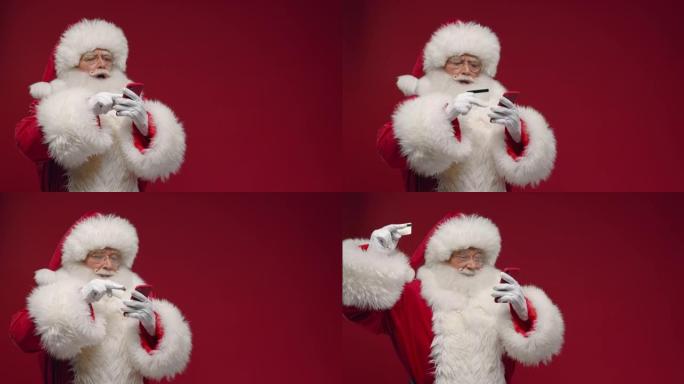 细心的圣诞老人在网上购物，在红色智能手机上输入卡号，然后庆祝购买成功，站在红色背景下并带有复印空间