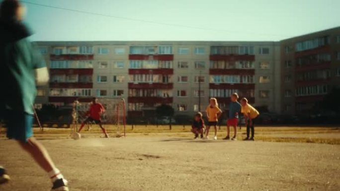 附近的孩子在城市后院外面踢足球。多元文化的朋友在郊区一起踢足球。小男孩点球，但错过了大门。低角度手持