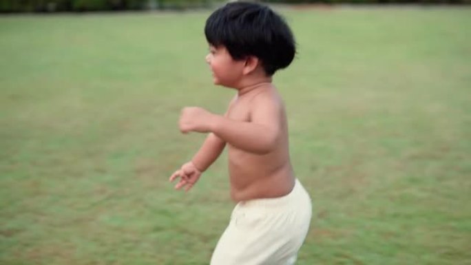 可爱的蹒跚学步的小男孩在乡村公园绿草丛中奔跑