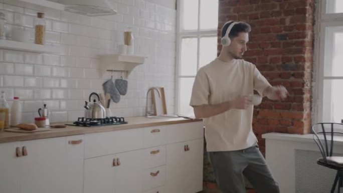 快乐的家伙在家里的现代厨房里跳舞喝咖啡和使用智能手机