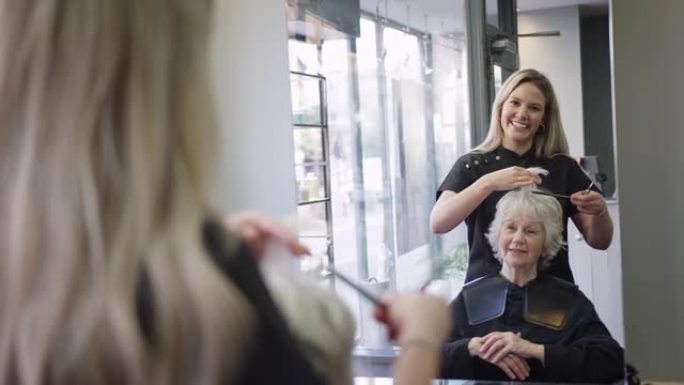 美发沙龙女发型师剪发的高级女性镜子中的反射