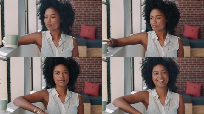 黑人妇女喝咖啡，放松身心，休息时在坐在窗前的创意平面设计公司微笑。南非女孩或年轻员工设计师微笑，在初