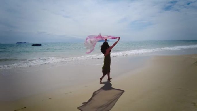 女人挥舞着围巾走在沙滩上