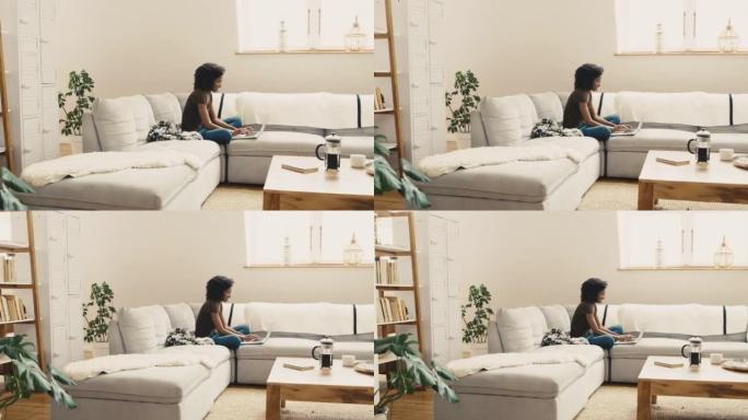 一名年轻的非洲裔美国妇女坐在家里的沙发上使用笔记本电脑。一位美丽的混血女性，非洲裔在客厅的沙发上放松
