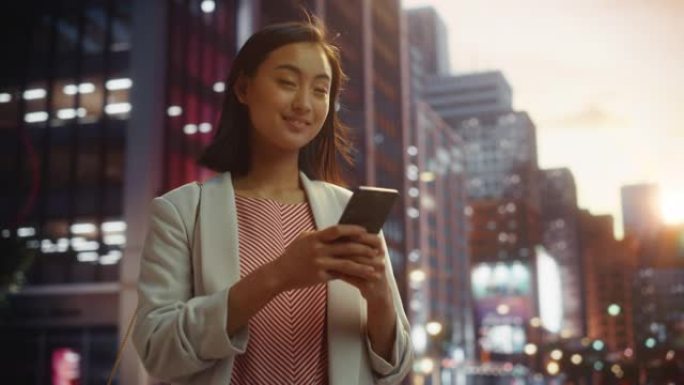 一位自信的日本女性在日落时穿着时髦的休闲服并使用智能手机的肖像。时尚的女人在网上与人联系，传递信息和
