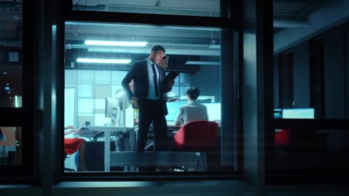 外面的镜头: 在办公室里用平板电脑工作的商人。经理站在窗户旁时在手机上交谈。员工计划财务任务和业务发