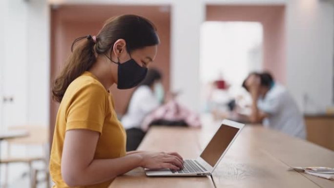 带防护面罩的自由职业者在咖啡馆的笔记本电脑上工作