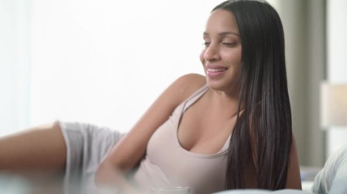 4k视频片段，一名年轻女子早上在家喝一杯水并在床上放松