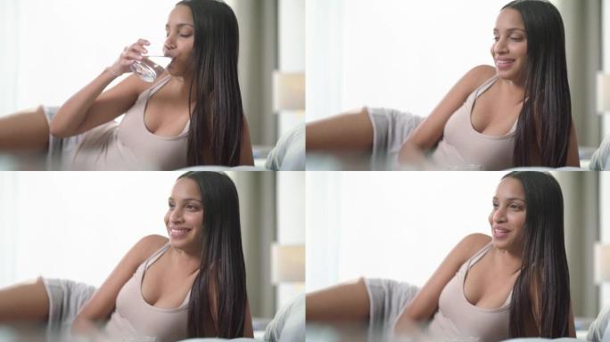 4k视频片段，一名年轻女子早上在家喝一杯水并在床上放松