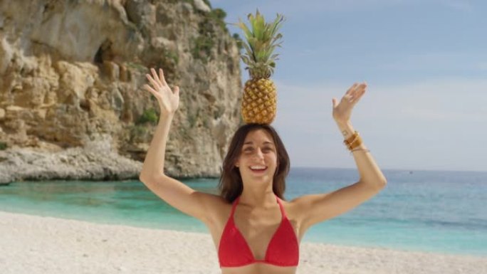 4k视频片段，两名迷人的年轻女性站在海滩上，试图平衡头上的菠萝