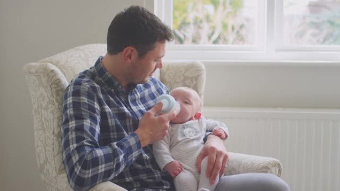 父亲一起在家里休息室的椅子上用奶瓶喂养小儿子
