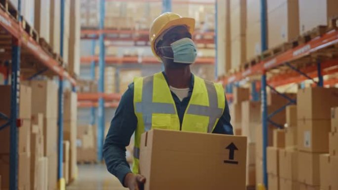 戴着医用口罩和安全帽的英俊男性工人的肖像背着纸板箱走过零售仓库，货架上摆满了货物。安全第一防护工作场