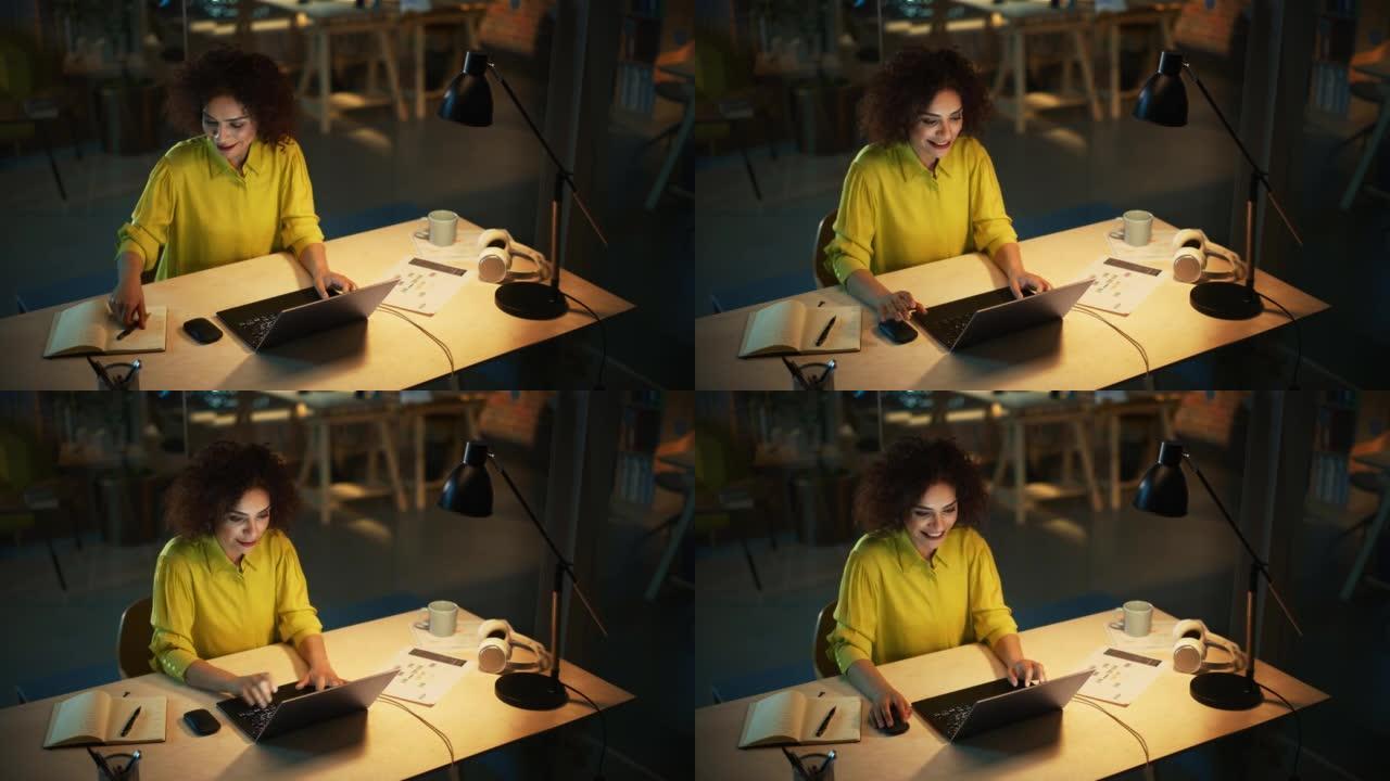 美丽的中东经理晚上坐在创意办公室的办公桌前。年轻时尚女性在营销机构使用笔记本电脑。在笔记本上写下重要