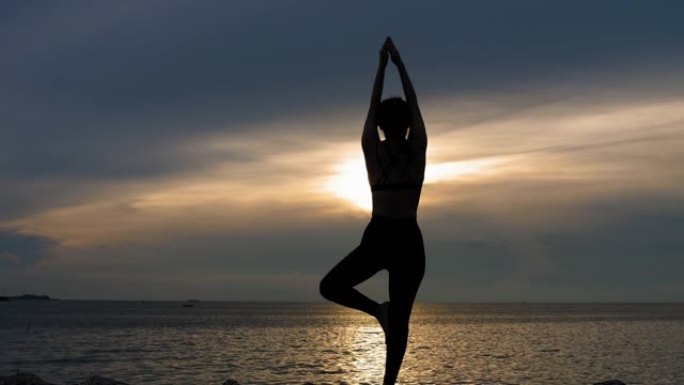 剪影女孩在日落时在海滩上摆树瑜伽姿势