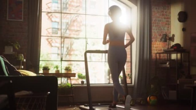 美丽的运动运动女人在家里的健身房跑步机上跑步。精力充沛的女性运动员训练，一边听播客，戴着耳机听音乐。