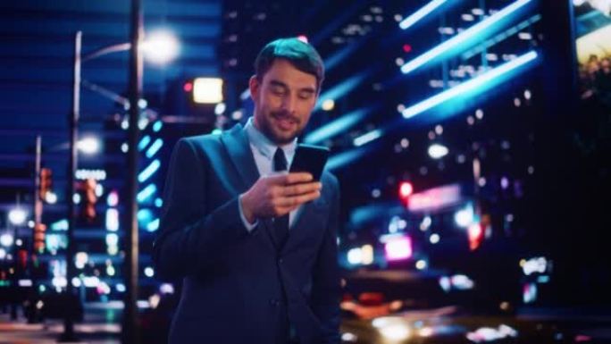一个穿着时髦西装的英俊男子的肖像在夜晚霓虹灯的现代城市街道上行走。有吸引力的男性使用智能手机，环顾城