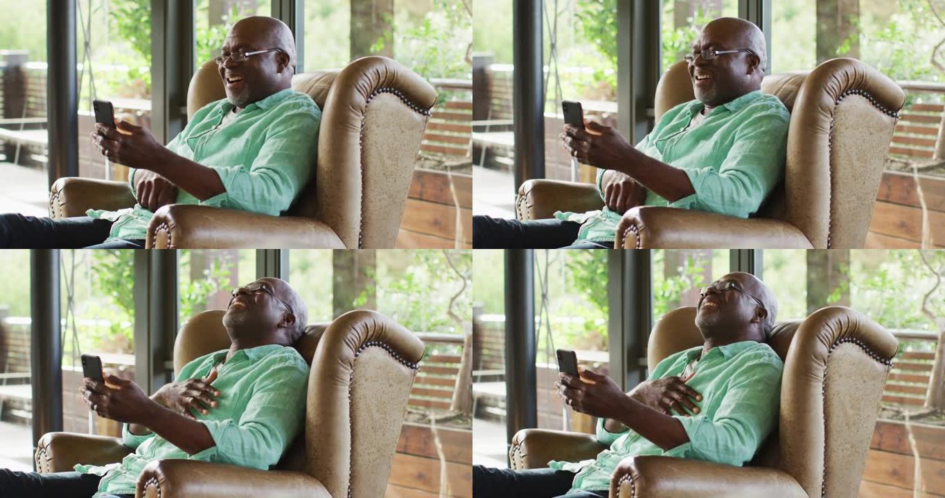 快乐的非洲裔美国高级男子坐在扶手椅上，用智能手机笑着
