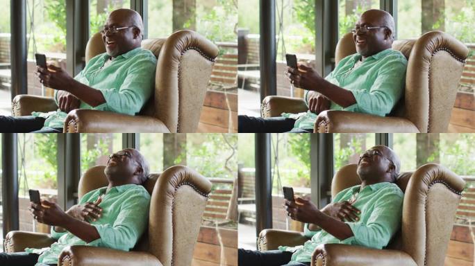 快乐的非洲裔美国高级男子坐在扶手椅上，用智能手机笑着