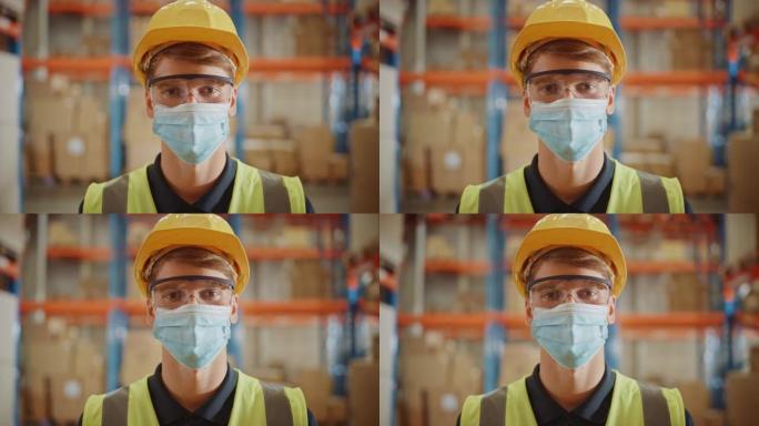 英俊的男性工人的肖像戴着医用口罩和安全帽，拿着纸板箱，站在装满货物的大型零售仓库中。安全第一防护工作