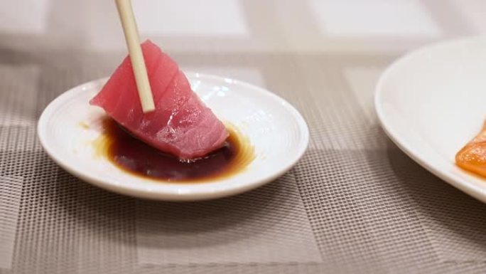 4K UHD慢动作手持: 用筷子将金枪鱼生鱼片浸入酱油碗中。日本美食美食，亚洲文化。健康食品概念。