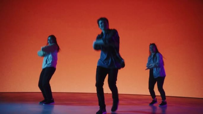 由三位时尚的专业舞者组成的多元化小组，在工作室环境中的虚拟制作过程中，在带有橙色背景的大Led墙屏幕