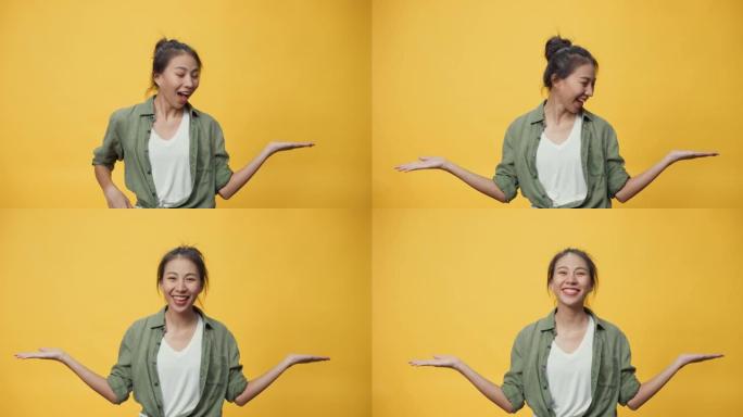 自信美女亚洲青年女士站在孤立的黄色背景上张开的手掌指向复制spac显示空旷的空间，展示广告微笑兴奋。