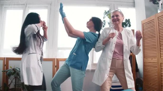 战胜疾病。三个有趣的多民族快乐女医生一起跳舞，庆祝诊所工作场所的成功。