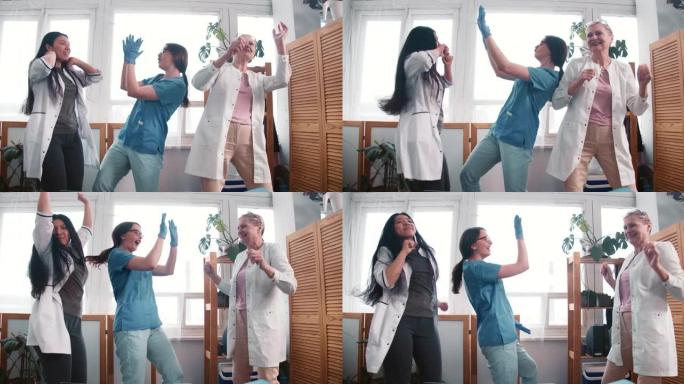 战胜疾病。三个有趣的多民族快乐女医生一起跳舞，庆祝诊所工作场所的成功。