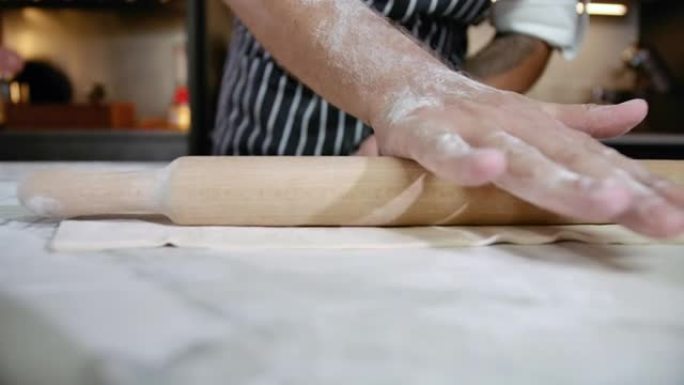 面包店的特写手在面团上使用木制Rolling面杖做饭。专业厨房的厨师用面粉准备糕点做面包。贝克滚动饼